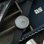Zenith chronograph watch with gray dial and black fabric strap on leather case and branded packaging.