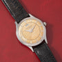A vintage Jaeger LeCoultre 'European Market' Powermatic dress watch with a textured beige dial, silver hour markers, power-reserve display, date window, and black leather strap displayed on a red textured surface.