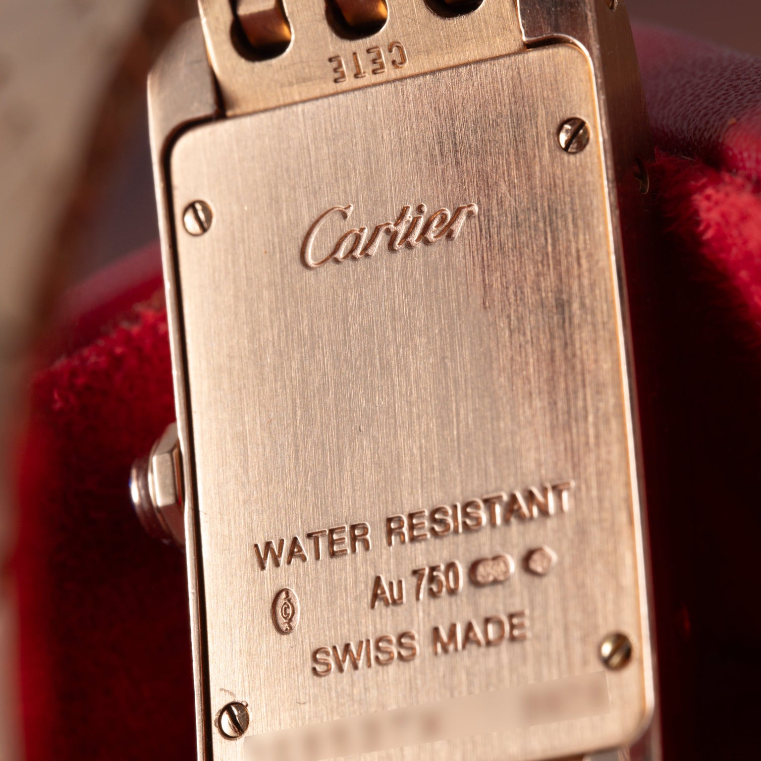 Close-up of the back of a Cartier Tank Americaine ladies watch in 18K rose gold, engraved with Cartier, WATER RESISTANT, Au 750, hallmarks, and SWISS MADE.