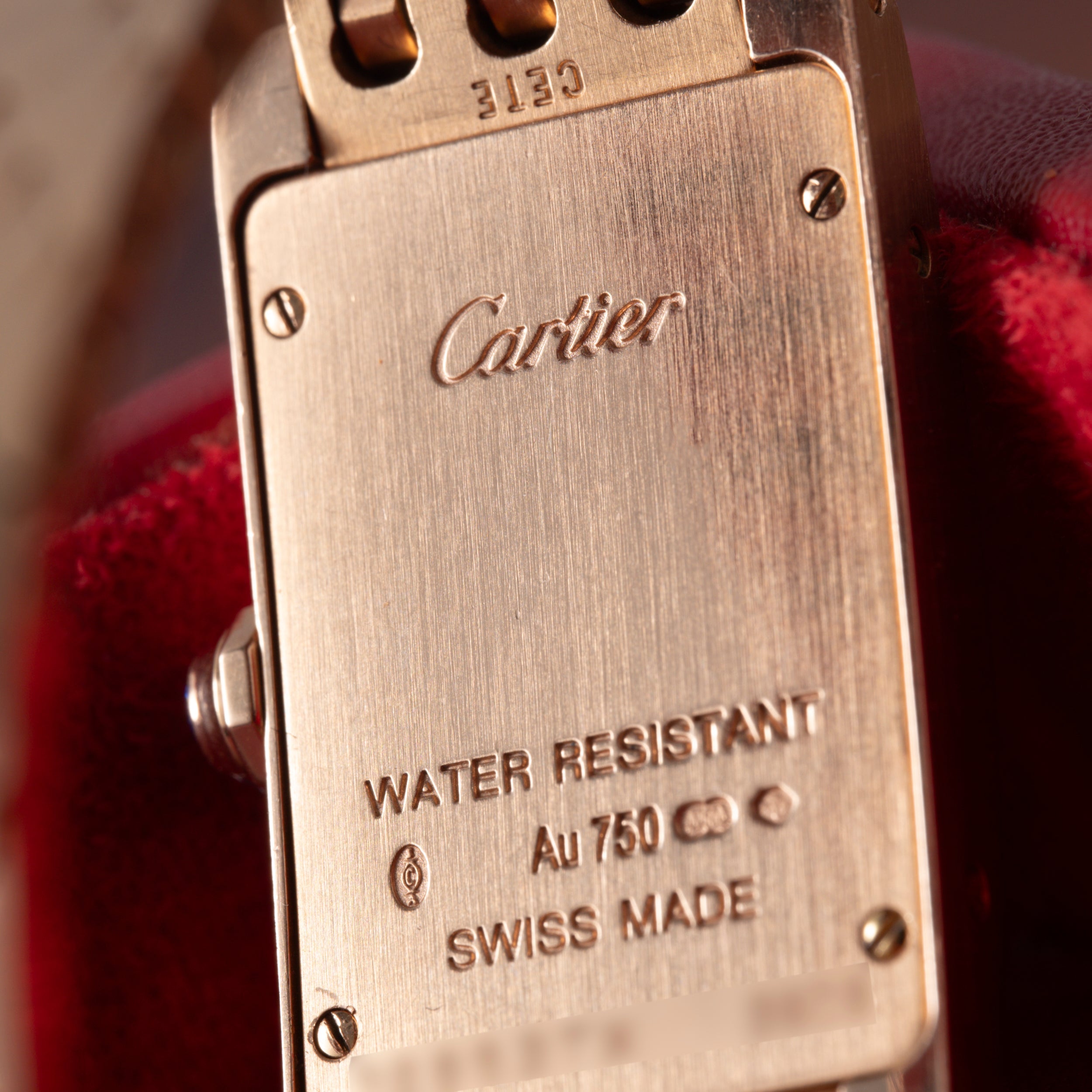Close-up of the back of a Cartier Tank Americaine ladies watch in 18K rose gold, engraved with Cartier, WATER RESISTANT, Au 750, hallmarks, and SWISS MADE.