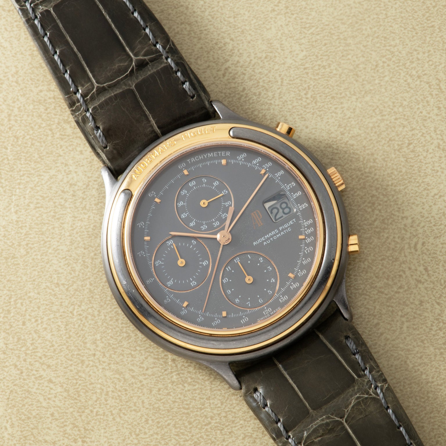 Two-tone chronograph watch with charcoal dial, three subdials, and black leather crocodile-embossed strap.