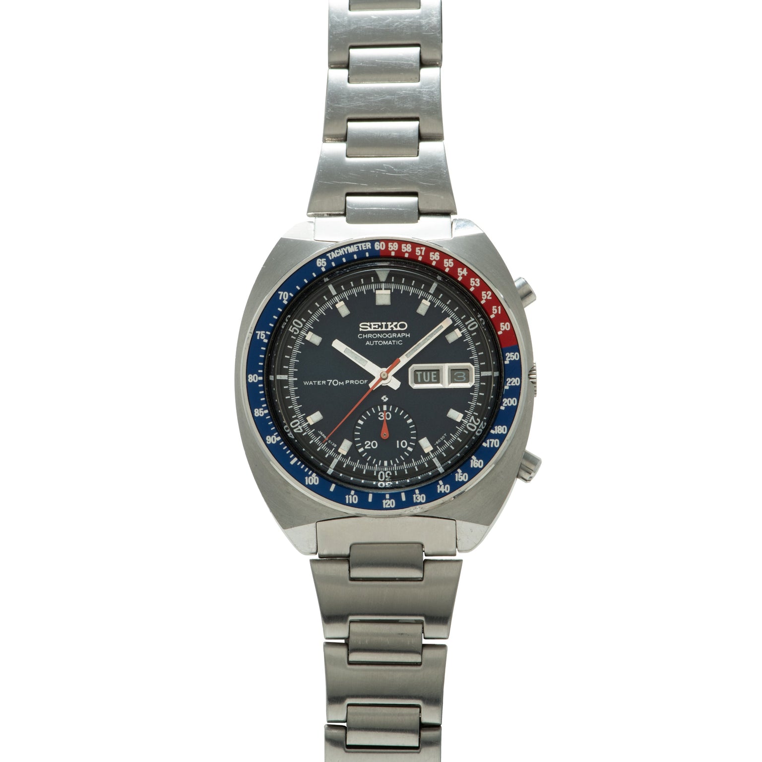 Seiko chronograph with black dial, blue and red tachymeter bezel, day-date window, and stainless steel bracelet.