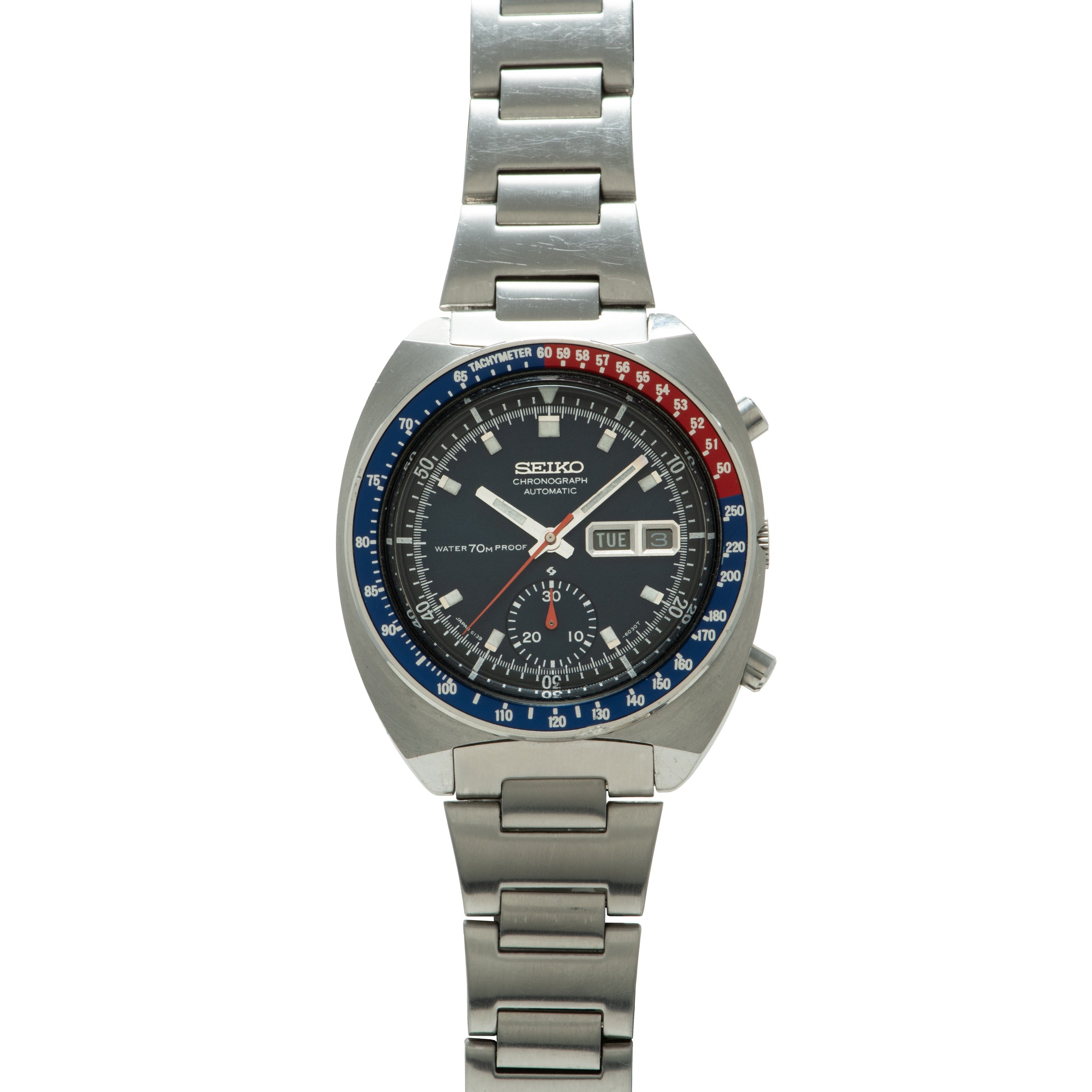 Seiko chronograph with black dial, blue and red tachymeter bezel, day-date window, and stainless steel bracelet.