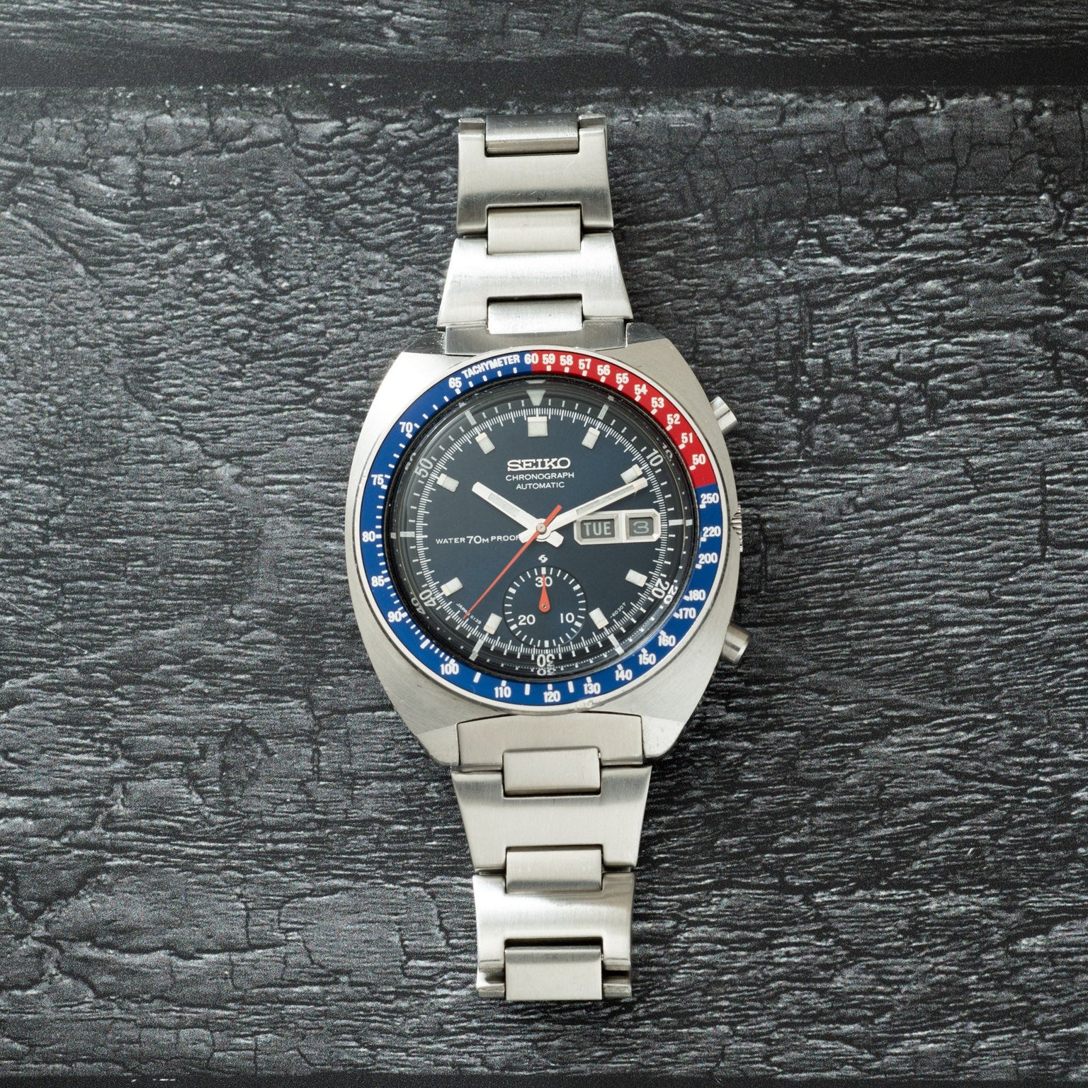 Seiko chronograph watch with stainless steel case and bracelet, black dial, blue and red bezel, and date window.