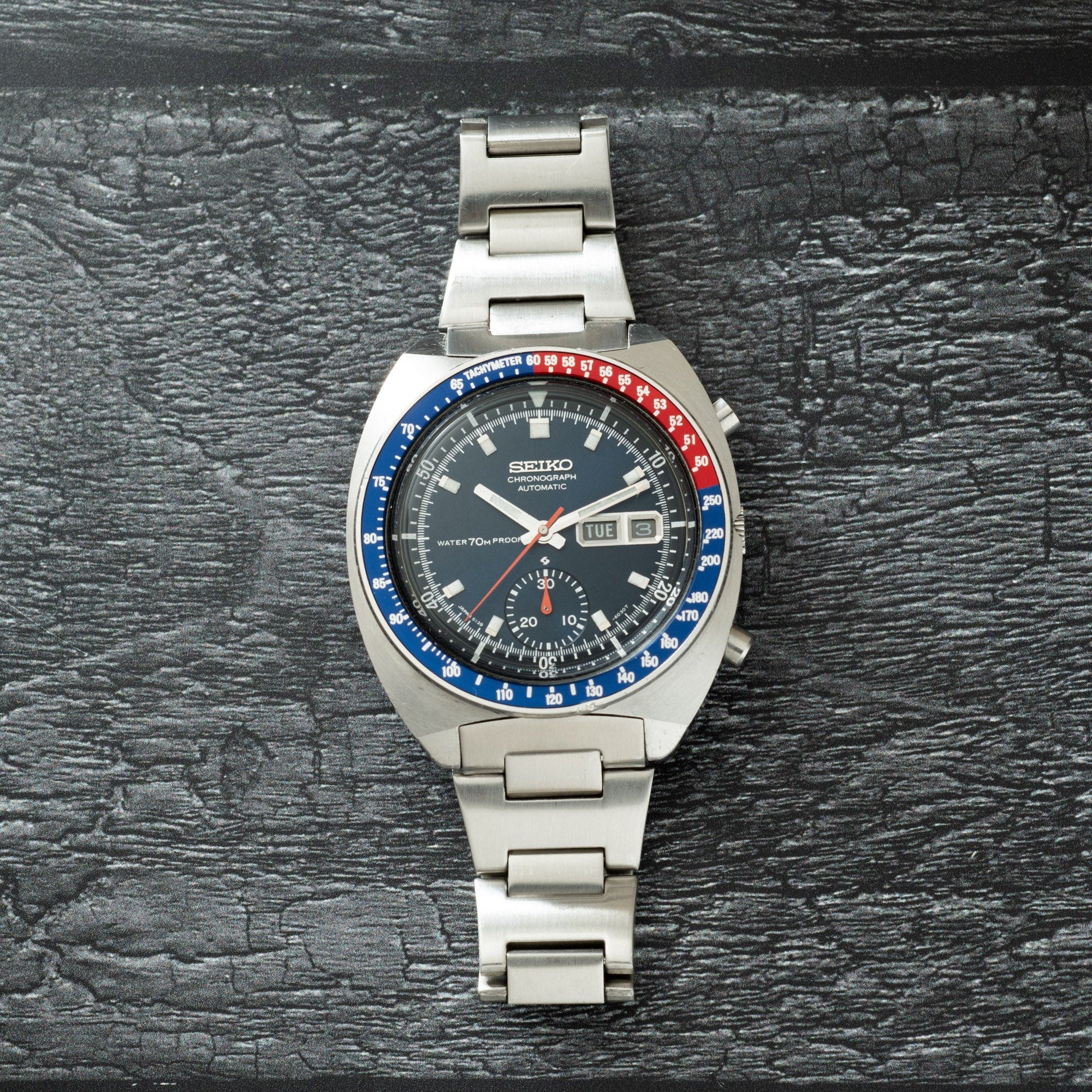 Seiko chronograph watch with stainless steel case and bracelet, black dial, blue and red bezel, and date window.