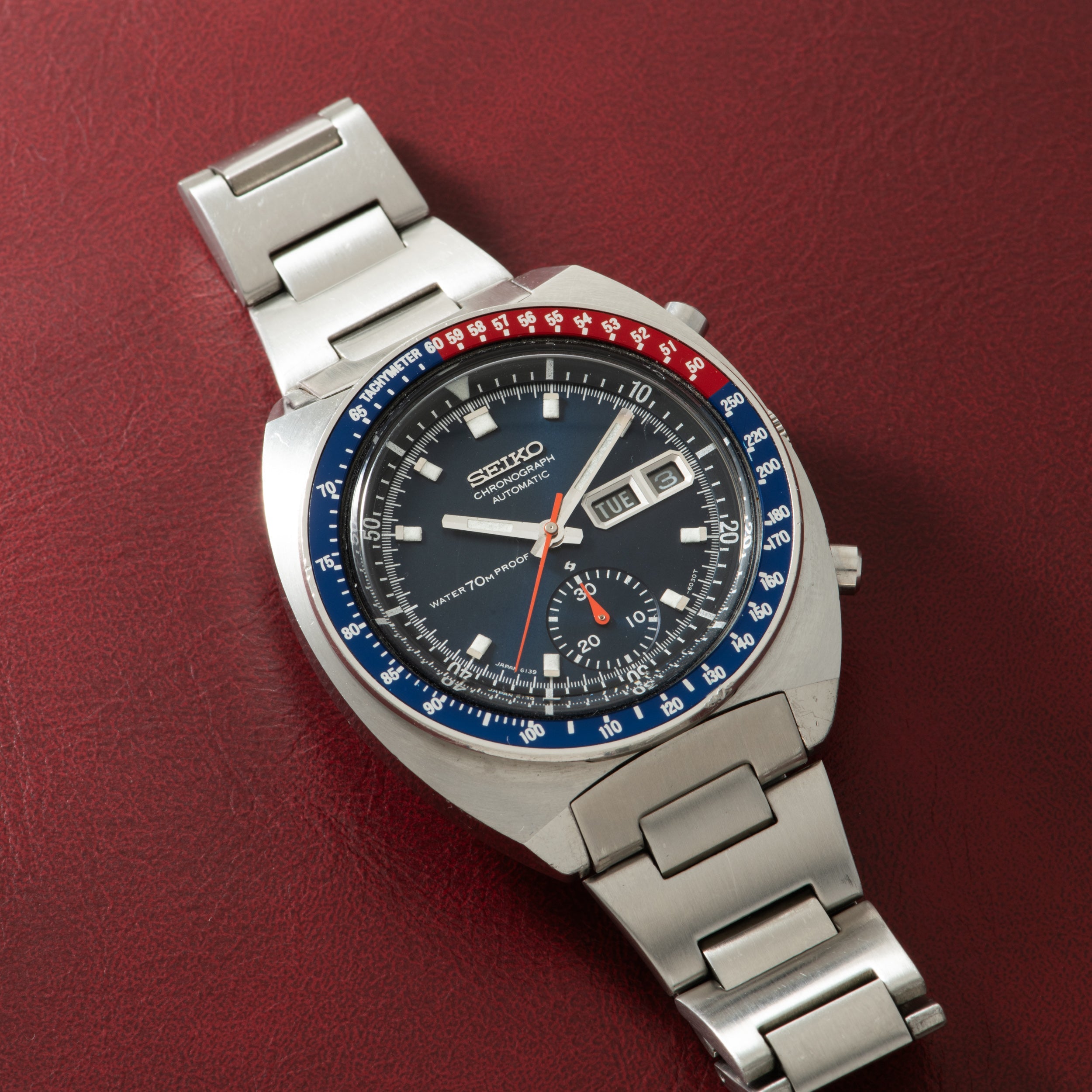 Seiko chronograph with stainless steel bracelet, black dial, blue and red tachymeter bezel, and date window.