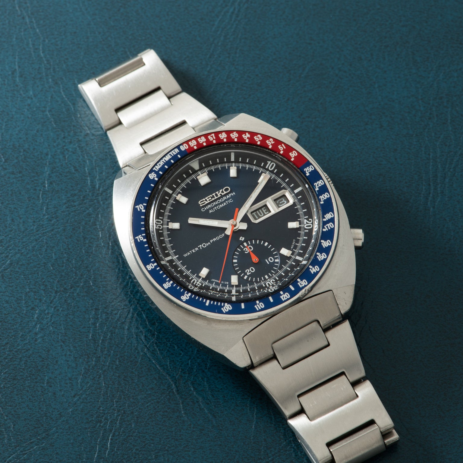 Seiko chronograph with stainless steel bracelet, black dial, blue and red bezel, and day-date window.