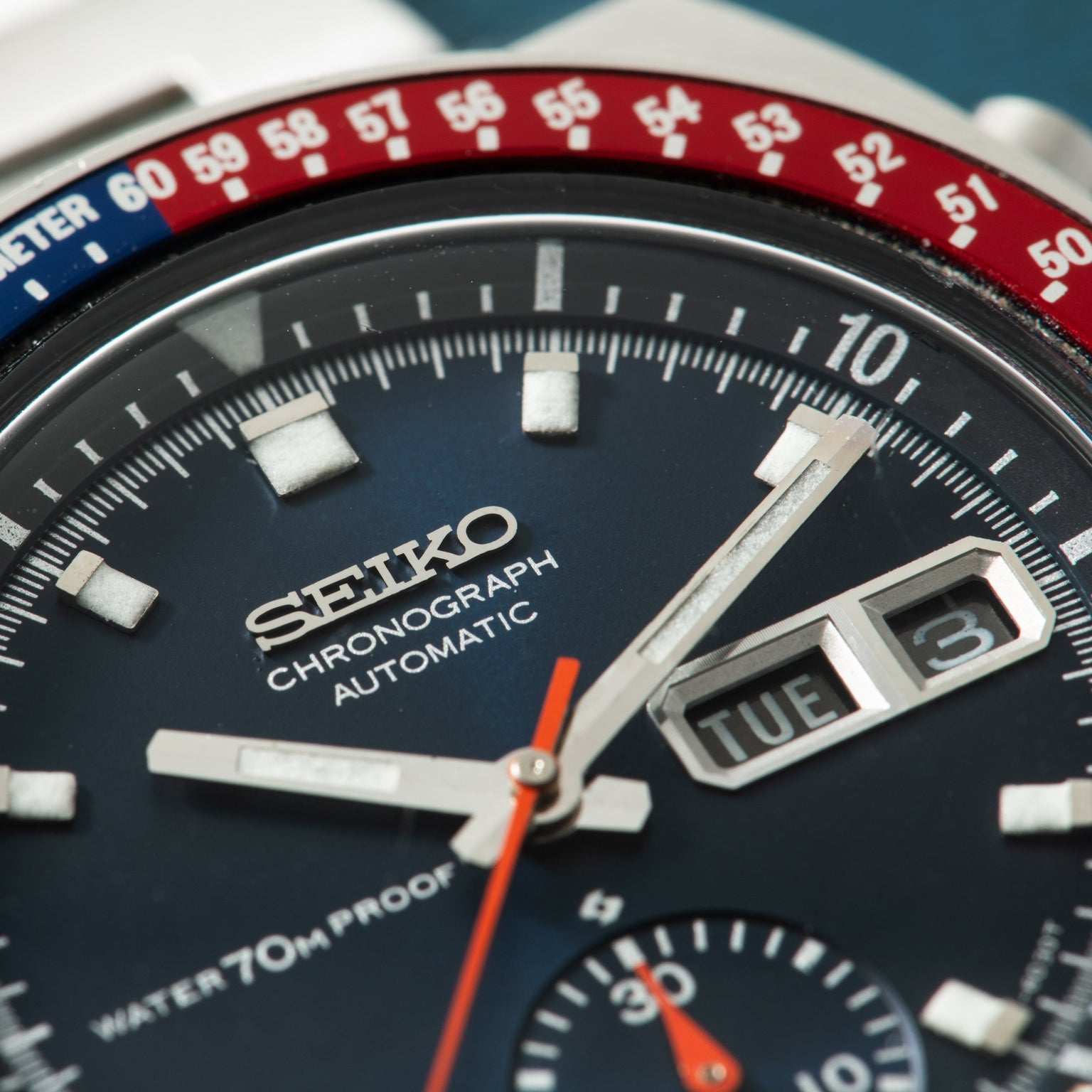 Seiko chronograph watch with blue dial, red and blue tachymeter bezel, white hour markers, and date window.