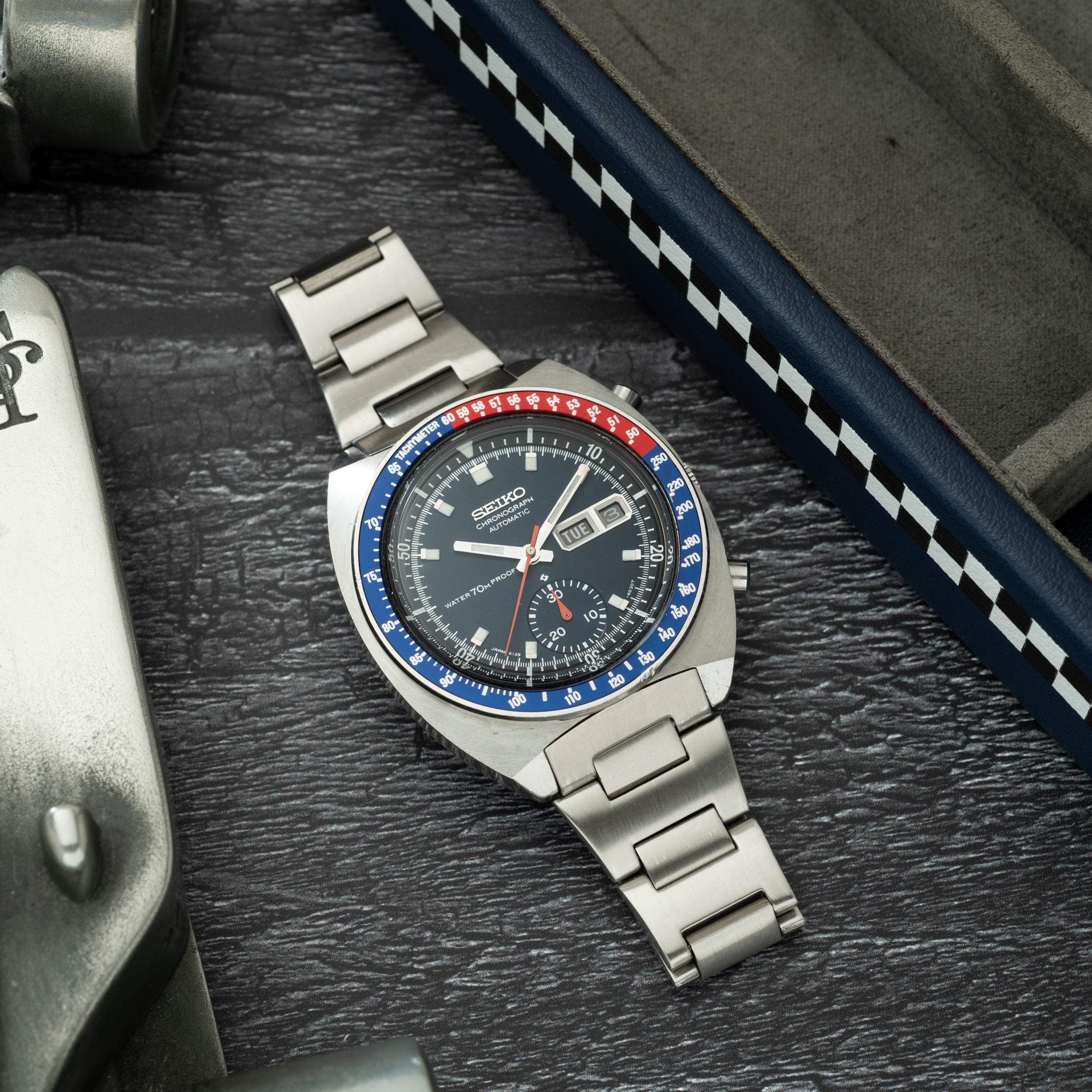 Seiko chronograph watch with stainless steel bracelet, black dial, blue and red bezel, and multiple subdials on dark wooden s