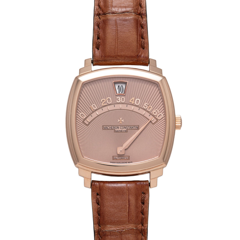 Rose gold tonneau watch with jump hour display, rose dial, and brown crocodile leather strap.