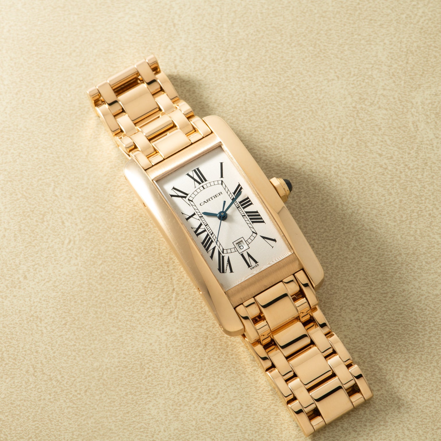 Gold-toned rectangular watch with white dial, Roman numerals, and linked bracelet band displayed on beige background.