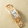 Gold-toned rectangular watch with white dial, Roman numerals, and linked bracelet band displayed on beige background.