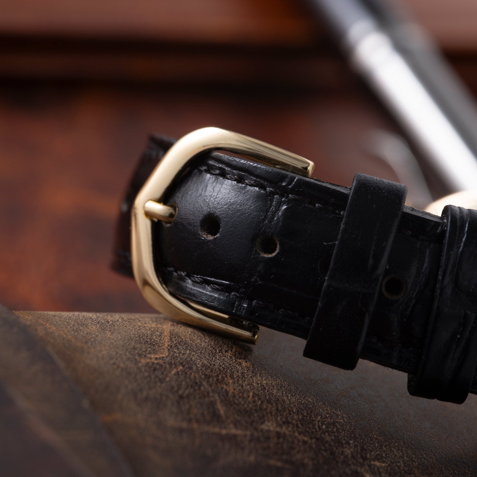 Gold-tone buckle on black leather strap with crocodile texture detail.