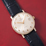Universal Geneve automatic watch with cream dial, gold-tone numerals and hands, date window, gold case, and black leather str