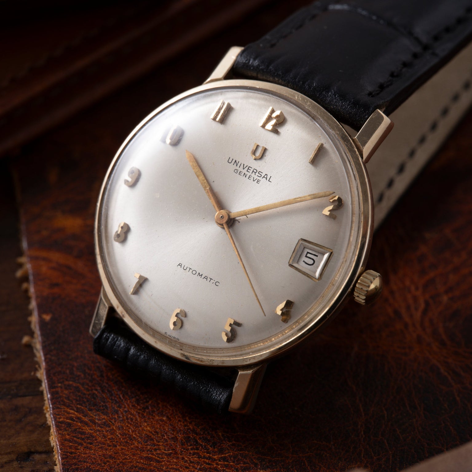 Universal Geneve automatic watch with silver dial, applied hour markers, date window, and black leather strap.