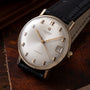 Universal Geneve automatic watch with silver dial, applied hour markers, date window, and black leather strap.