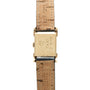 Gold-tone rectangular watch case with hooded lugs attached to tan crocodile leather strap.