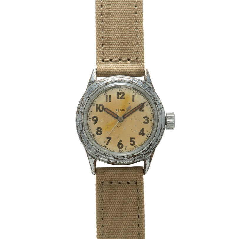 Elgin military watch with weathered steel case, cream dial with Arabic numerals, and tan fabric strap.
