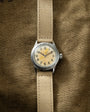 Elgin watch with cream dial, Arabic numerals, and tan canvas strap on olive fabric background.