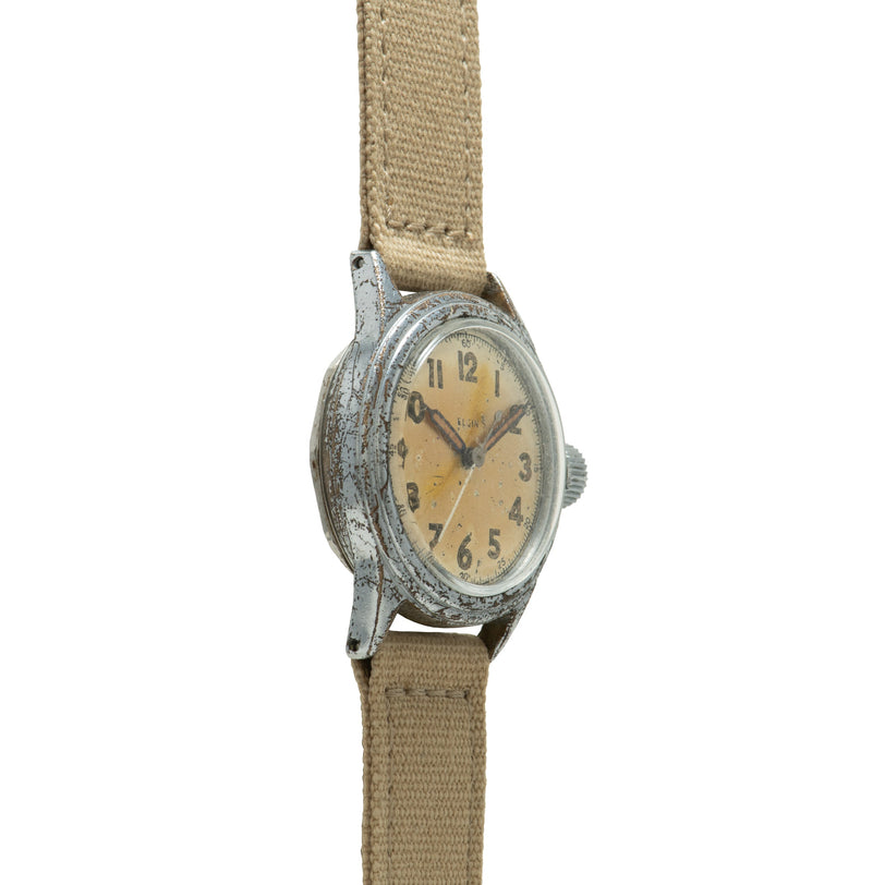 Vintage Elgin watch with patinated silver case, cream dial, Arabic numerals, and tan canvas strap.
