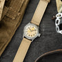 Elgin watch with cream dial and Arabic numerals on tan canvas strap, displayed on dark surface with military gear.