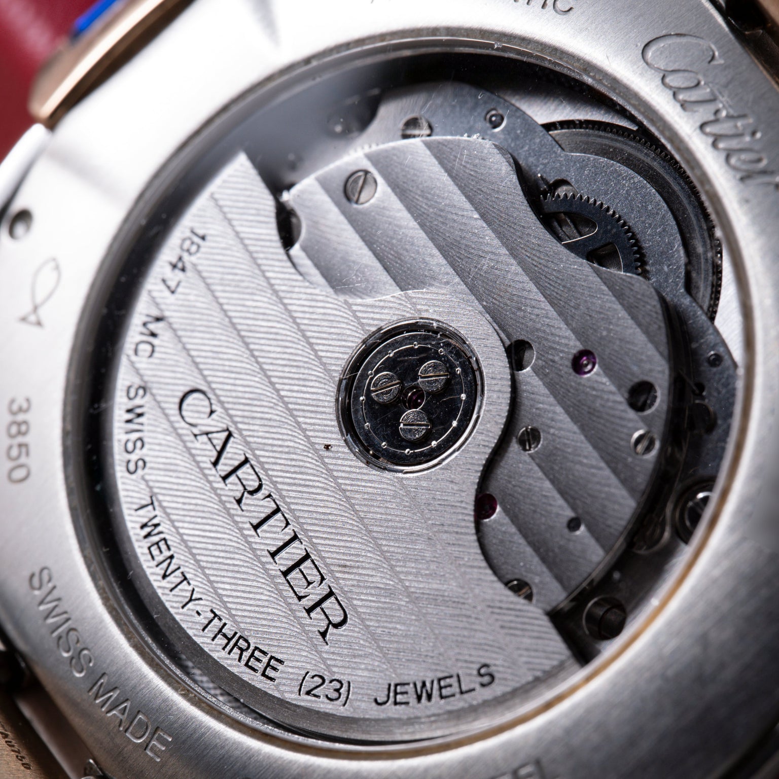 Close-up of automatic watch movement with engraved rotor, visible gears, and "Cartier" branding on brushed metal plate.