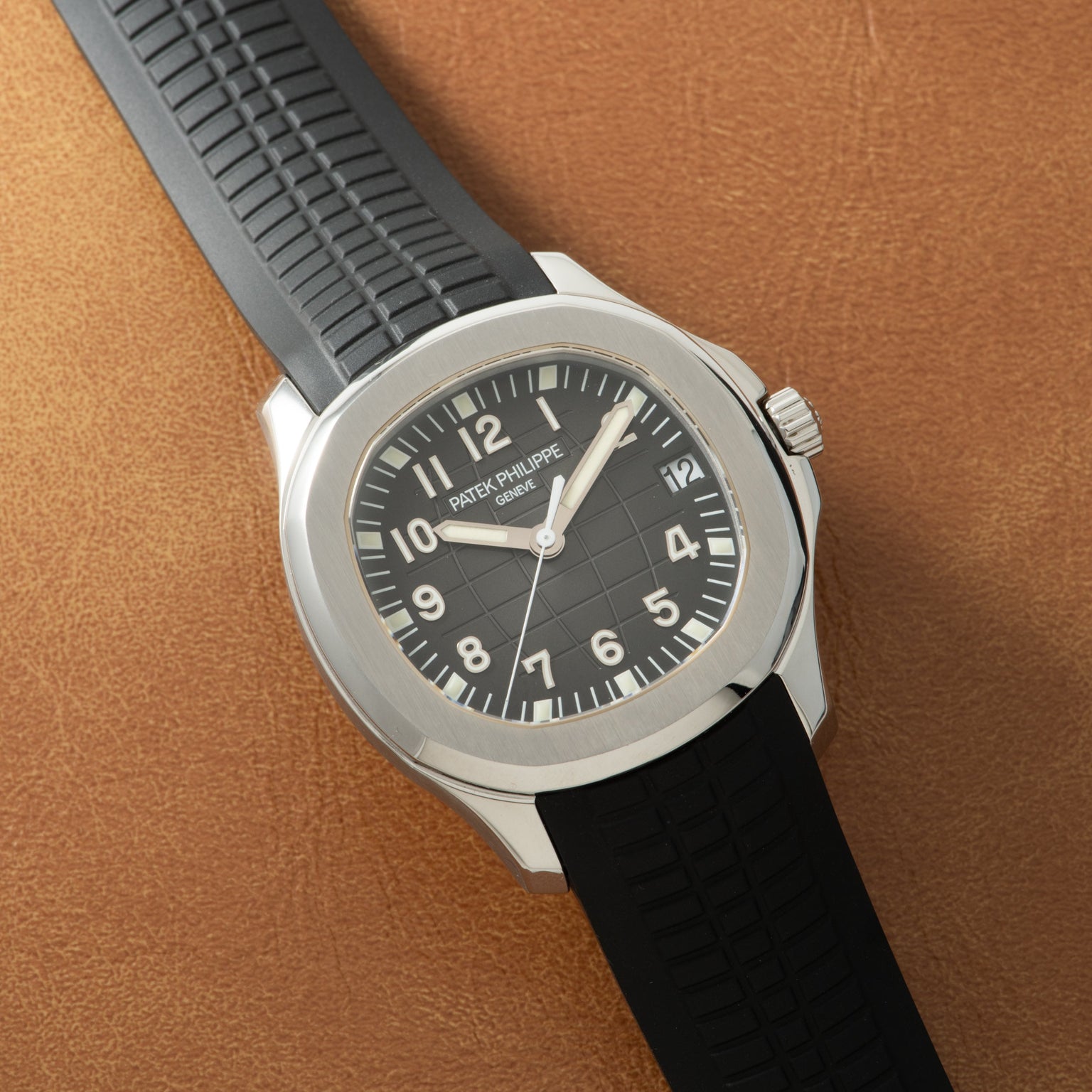 Stainless steel watch with black dial, Arabic numerals, and black rubber strap on tan leather background.