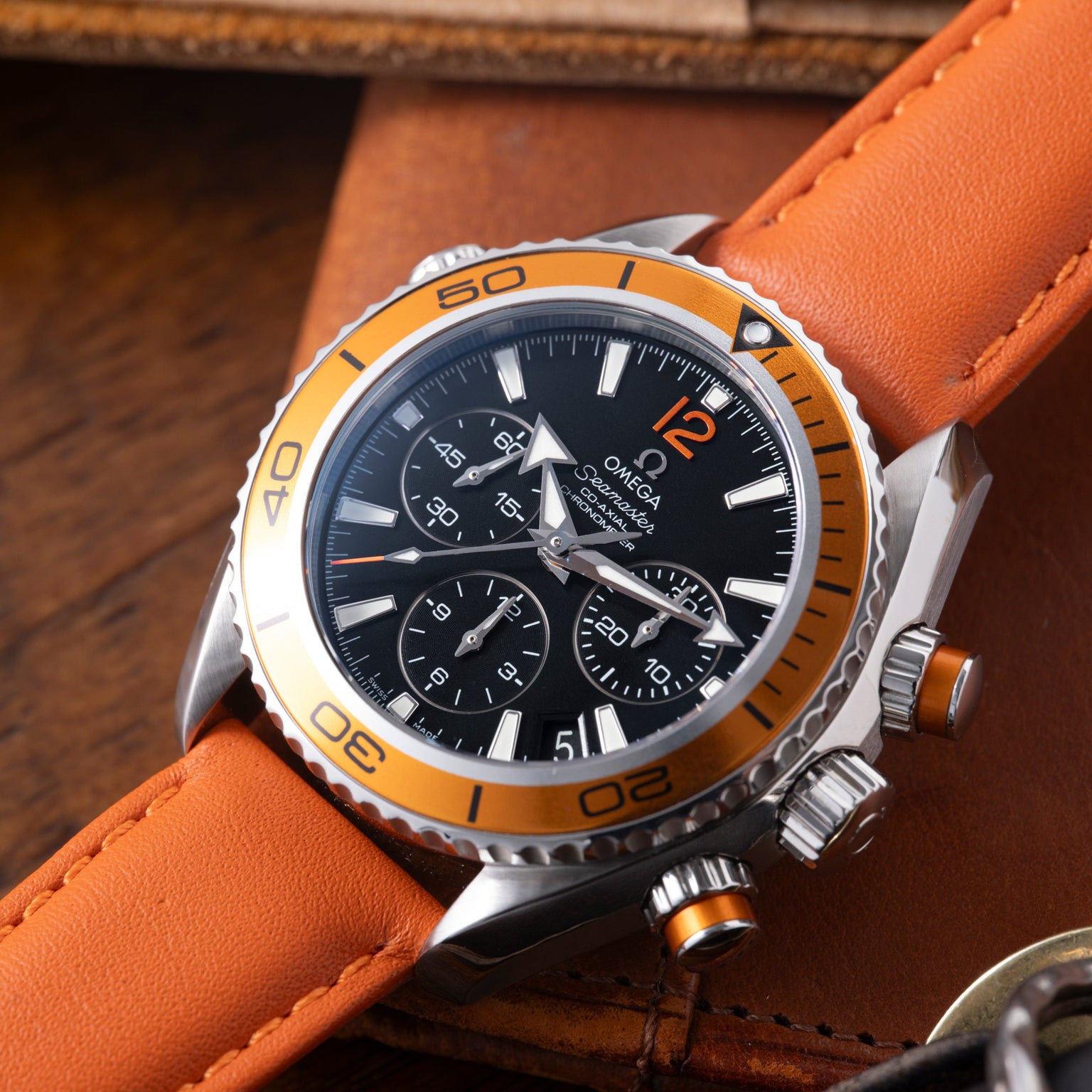 Stainless steel chronograph watch with orange bezel and black dial on orange leather strap.
