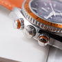 Stainless steel watch with orange bezel, dial, and accents, featuring chronograph pushers and textured bezel ring.