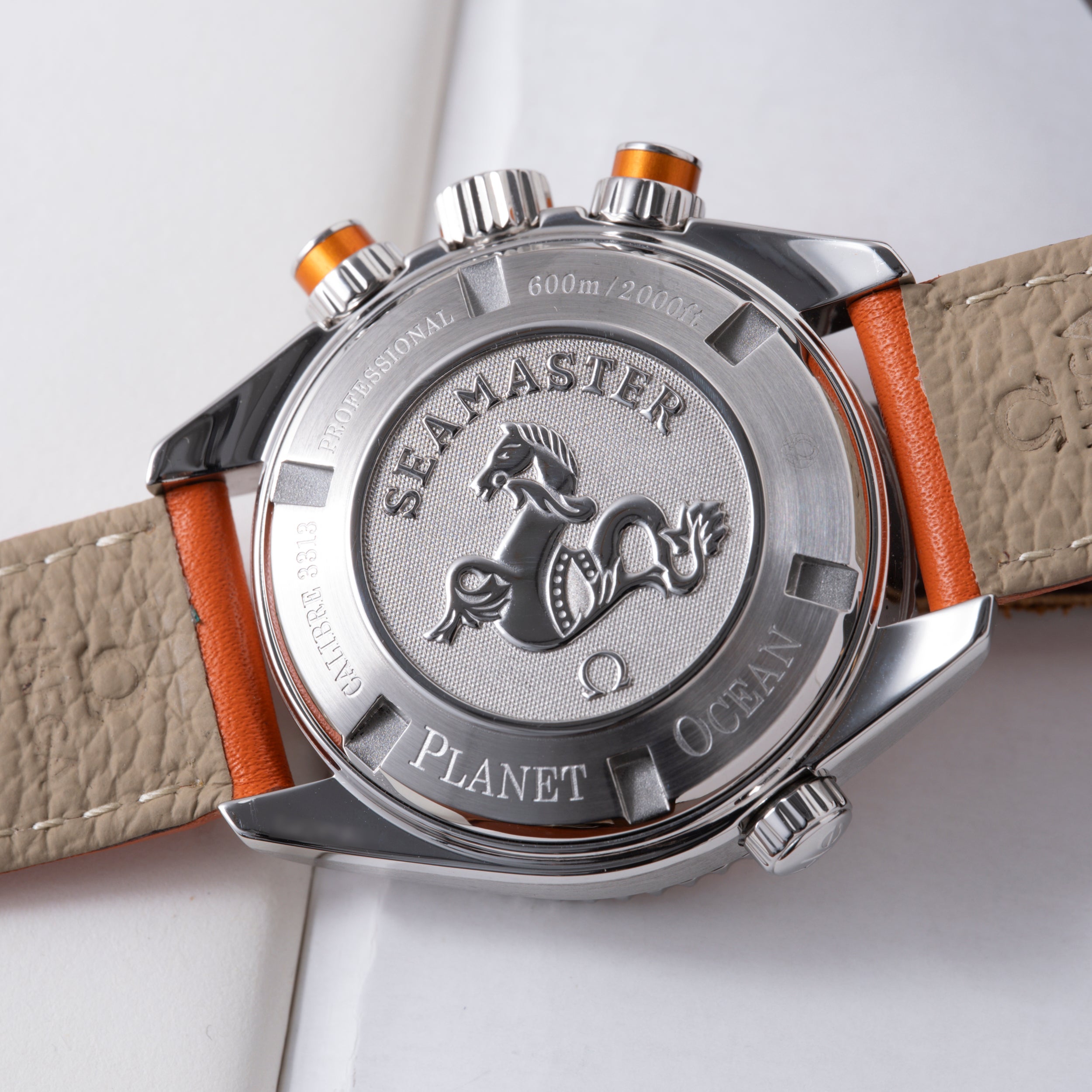 Stainless steel chronograph watch with orange and beige leather strap, showing caseback with seahorse emblem and 600m depth r