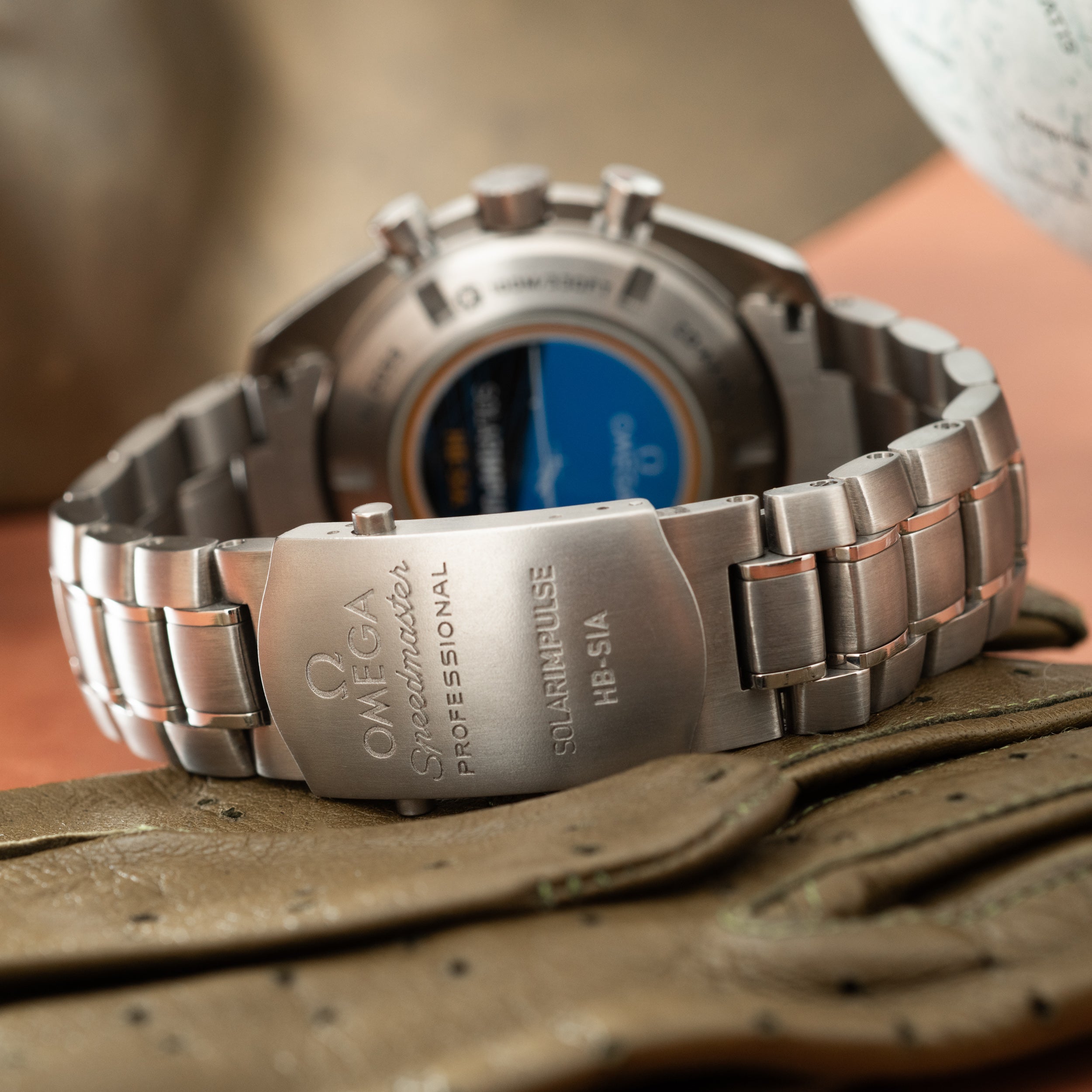 Titanium chronograph watch with blue dial and metal bracelet, shown from rear view on wood surface.