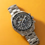 Titanium chronograph watch with black dial, tachymeter bezel, and three subdials on yellow background.