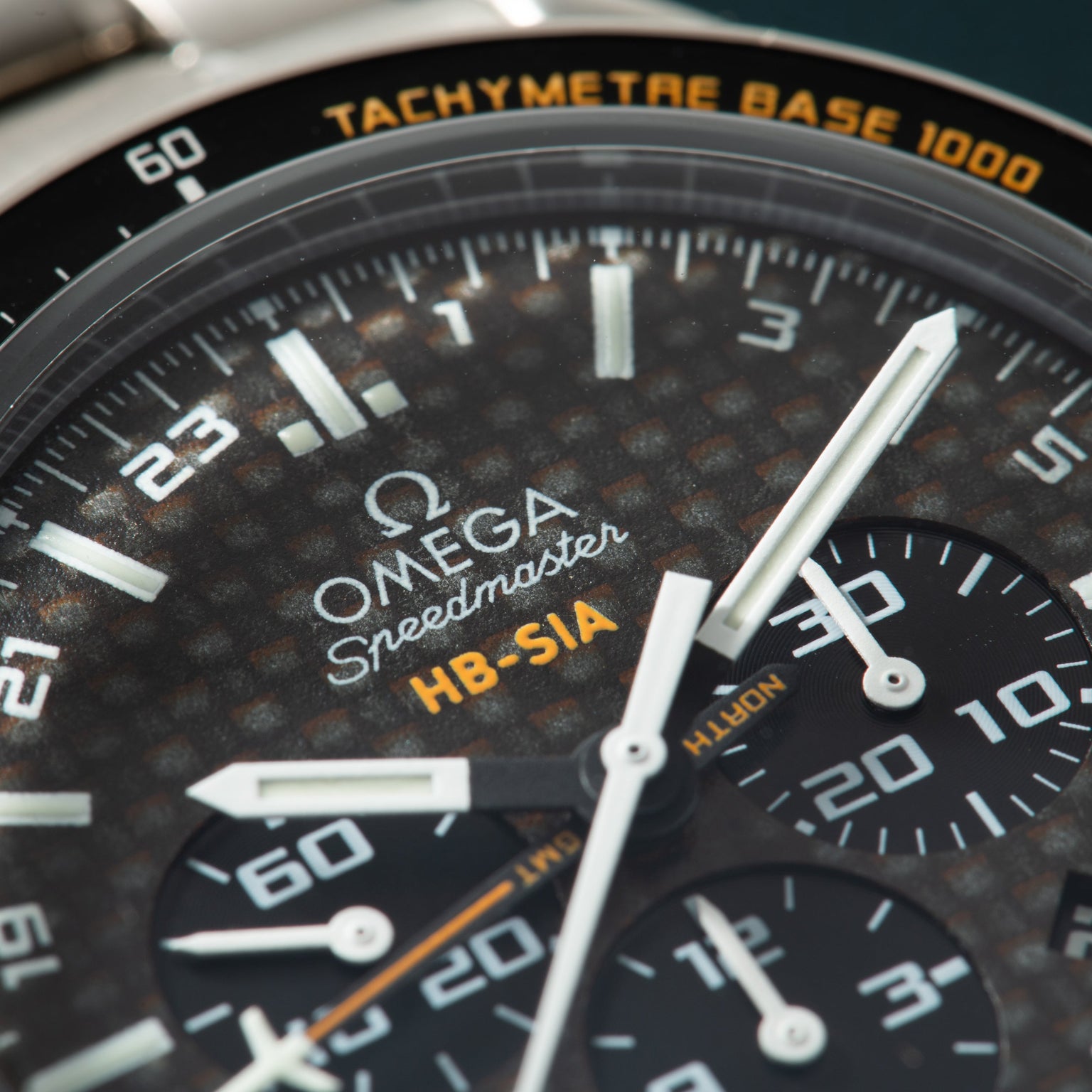 Close-up of Omega Speedmaster chronograph watch with dark dial, tachymetre bezel, and subdials showing wear.