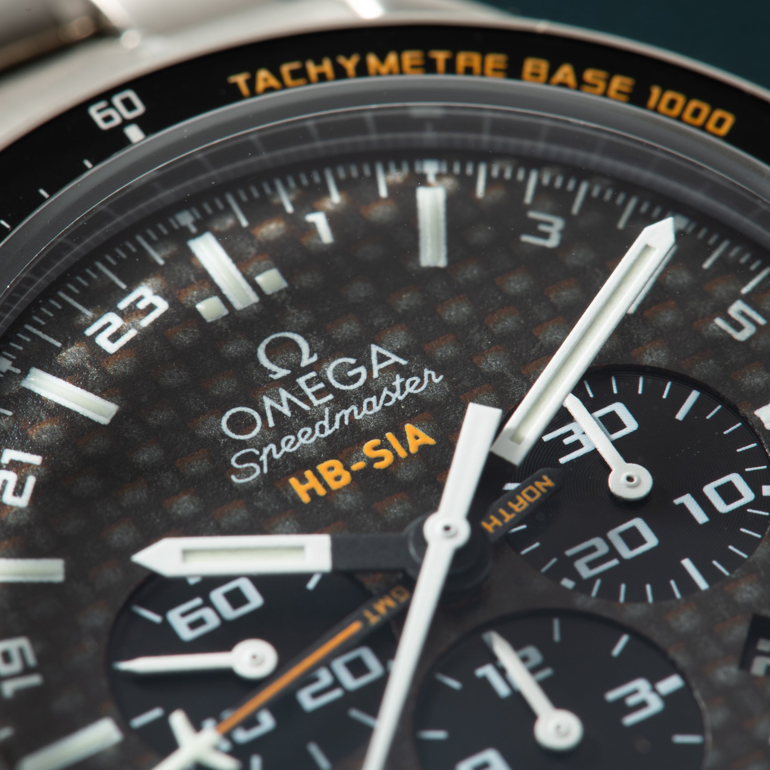 Close-up of Omega Speedmaster chronograph watch with dark dial, tachymetre bezel, and subdials showing wear.