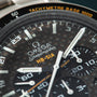 Close-up of Omega Speedmaster chronograph watch with dark dial, tachymetre bezel, and subdials showing wear.