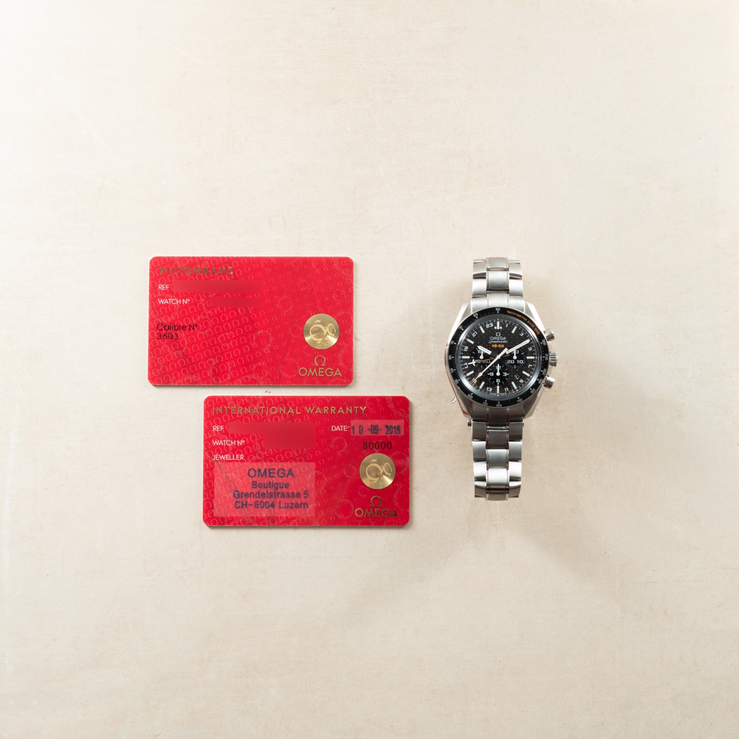 Omega Speedmaster titanium chronograph with black dial and three subdials, displayed with two red warranty cards.