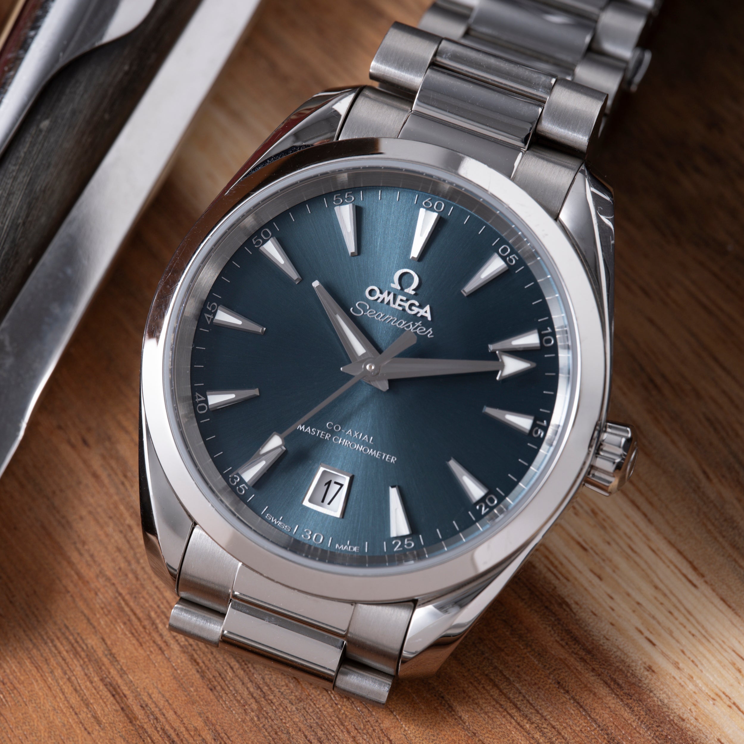 Omega Seamaster watch with blue dial, silver hands, date window, stainless steel case and bracelet on wooden surface.