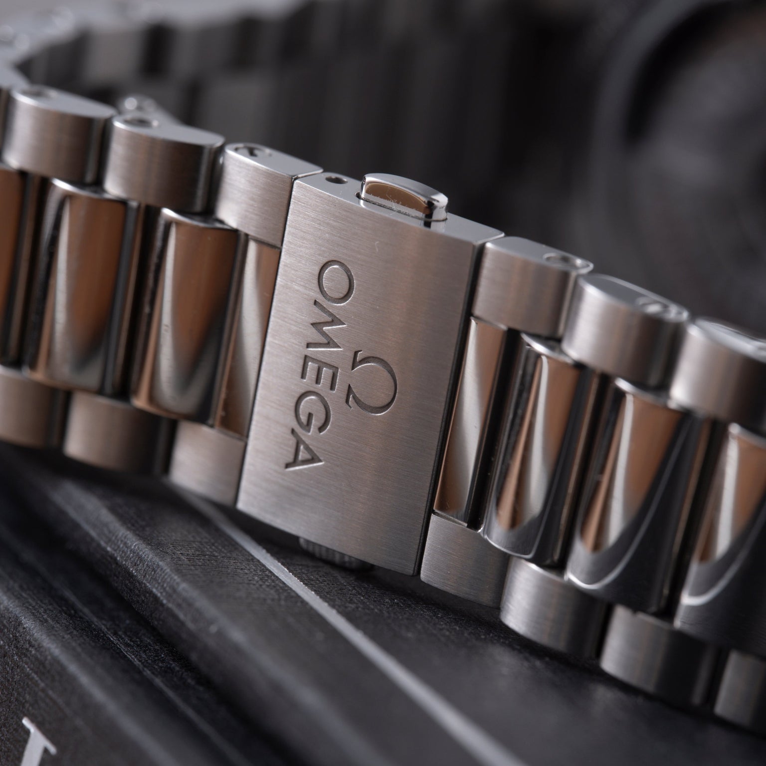 Stainless steel watch bracelet with Omega logo engraved on clasp, shown at angle on dark surface.