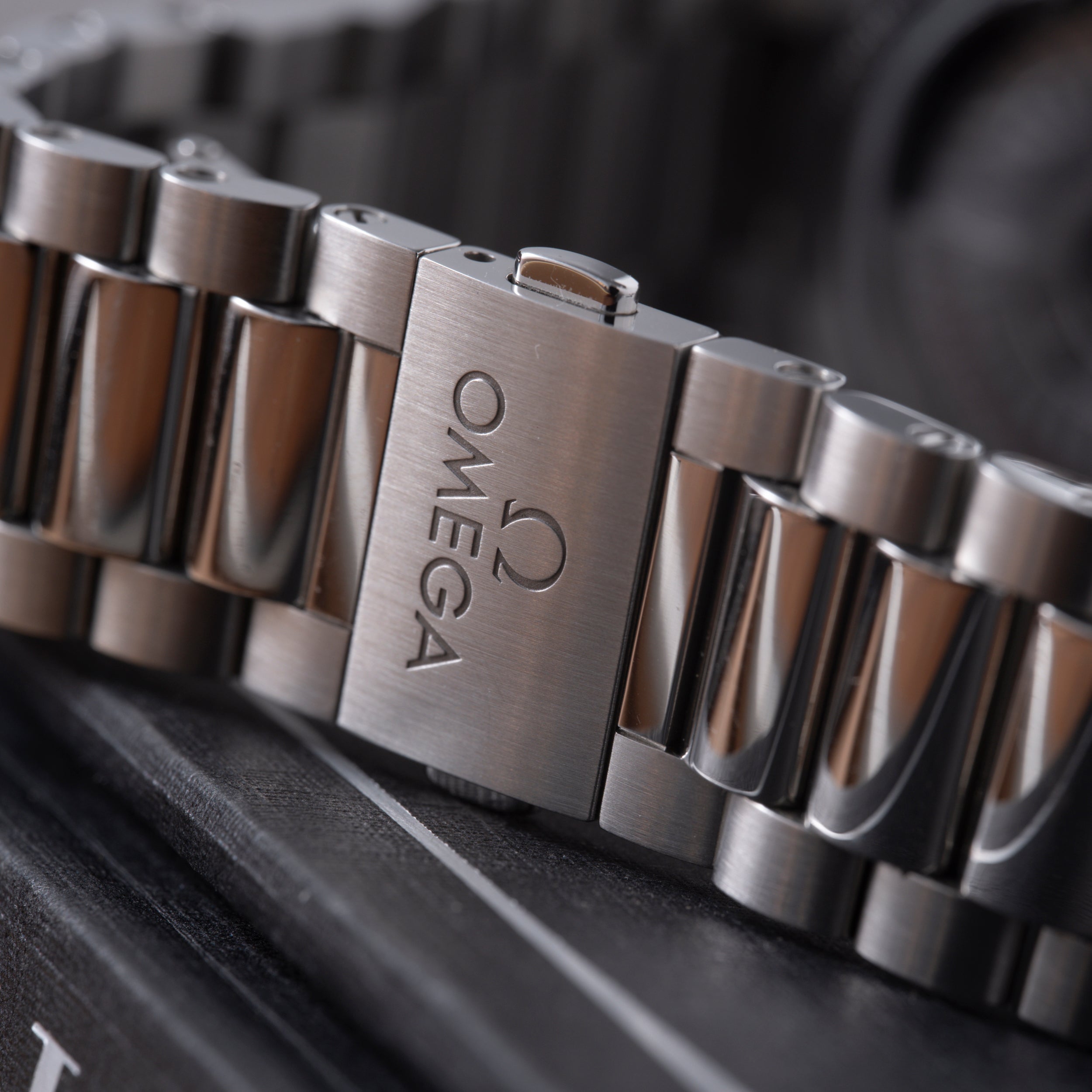 Stainless steel watch bracelet with Omega logo engraved on clasp, shown at angle on dark surface.