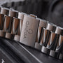 Stainless steel watch bracelet with Omega logo engraved on clasp, shown at angle on dark surface.