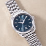 Stainless steel watch with dark blue dial, white hour markers and hands, date window, and matching metal bracelet.