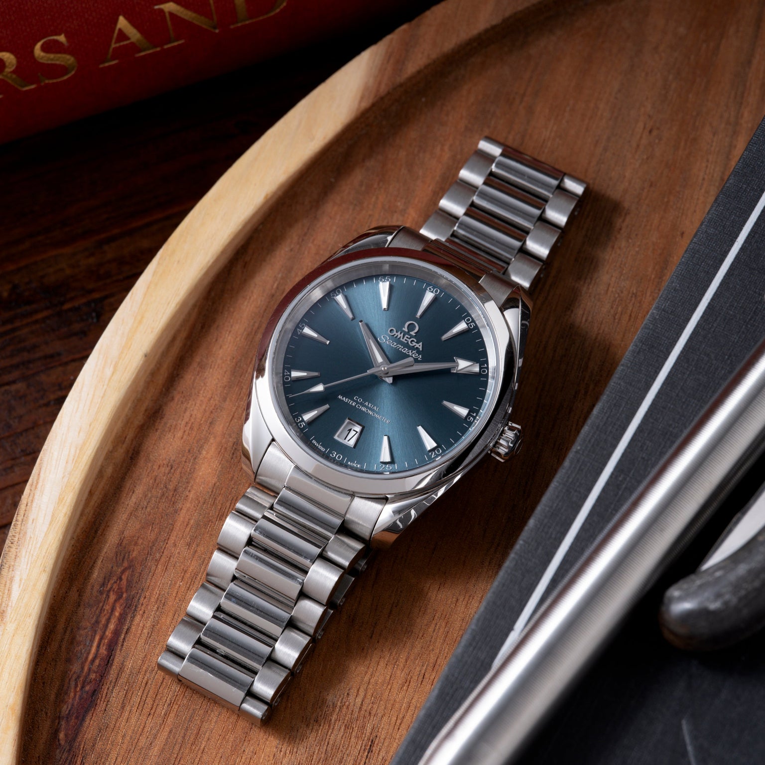 Omega Seamaster Aqua Terra watch with blue dial, silver bracelet, and date window on wooden surface.