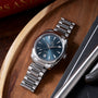 Omega Seamaster Aqua Terra watch with blue dial, silver bracelet, and date window on wooden surface.
