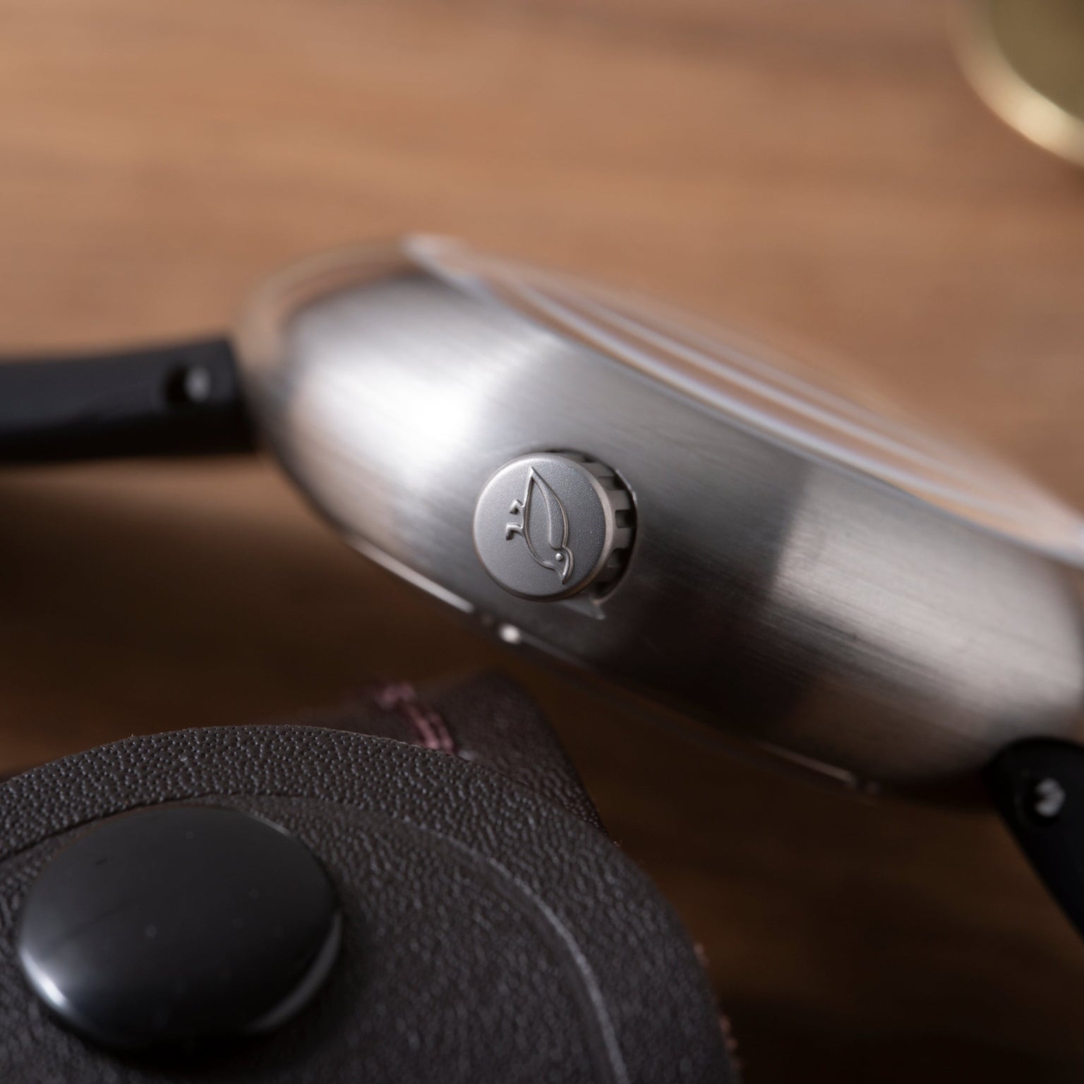 Brushed metal Ikepod Megapod watch with hourglass-shaped crown and black leather strap detail visible.