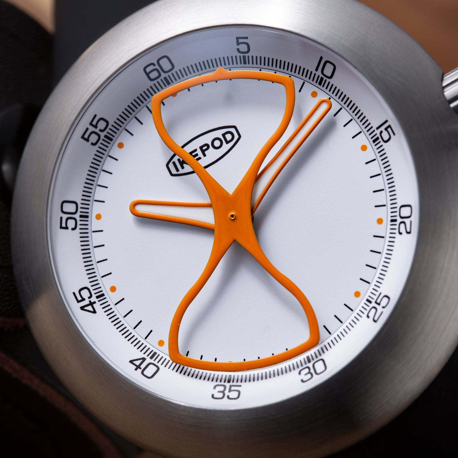 Ikepod Megapod timer with hourglass-shaped orange hands on white dial with numbered minute markings and brushed metal casing.