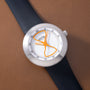 White Ikepod watch with orange hourglass-shaped hands and numerals on dial, dark blue rubber strap.
