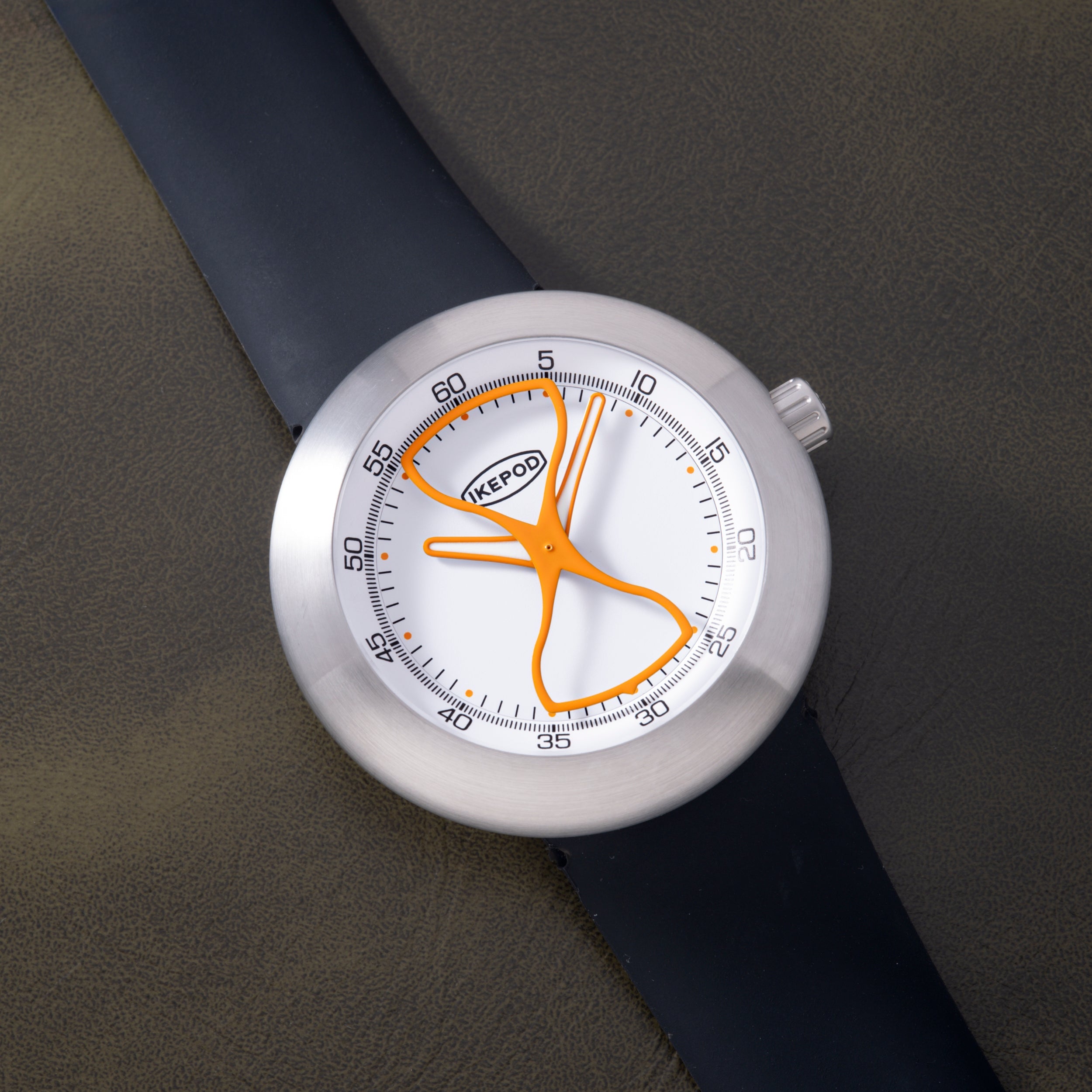White Ikepod watch with orange hourglass-shaped hands and markers, dark blue rubber strap, stainless steel case.