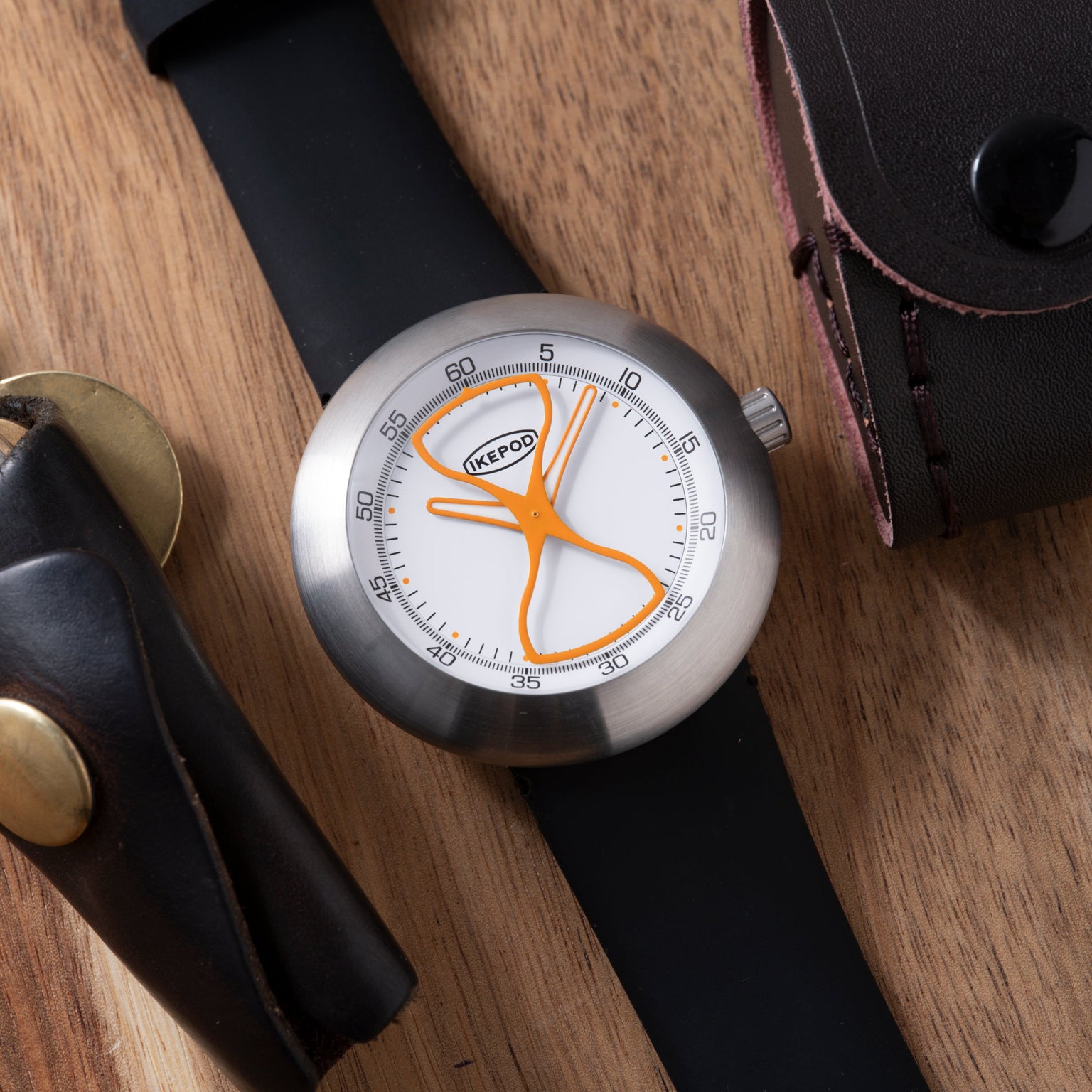 Ikepod Megapod watch with hourglass-shaped orange hands and dial on black leather strap.
