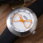 Ikepod Megapod watch with brushed steel case, white dial, orange hourglass-shaped hands, and black leather strap.