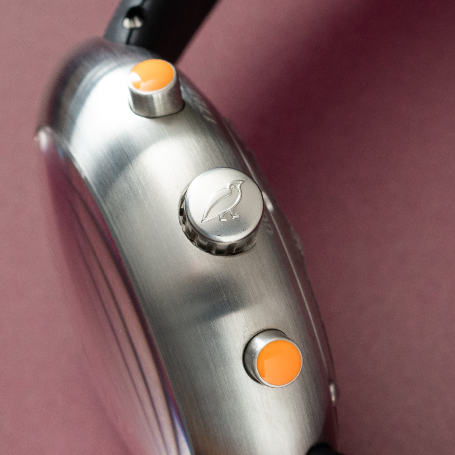 Brushed steel chronograph watch with orange pushers and bird engraving on center button, angled side view.